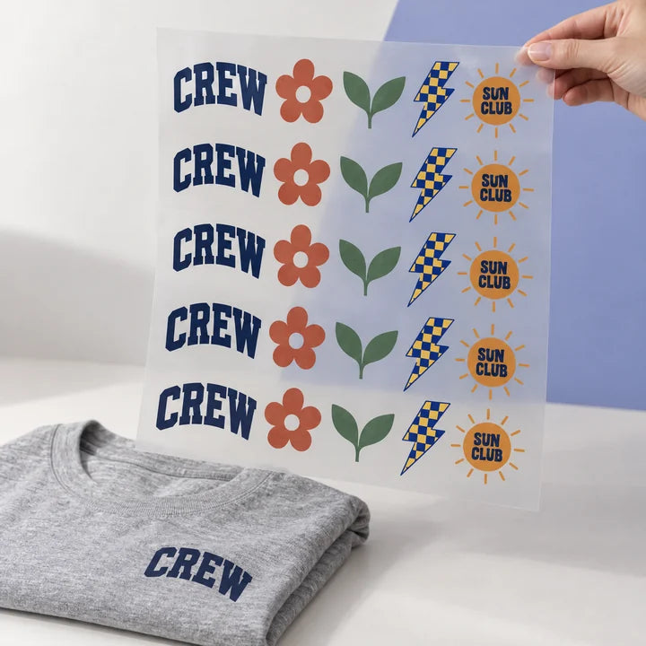 Mockup: hand holding up a finished DTF gang sheet of designs, with a grey T-shirt as an application example
